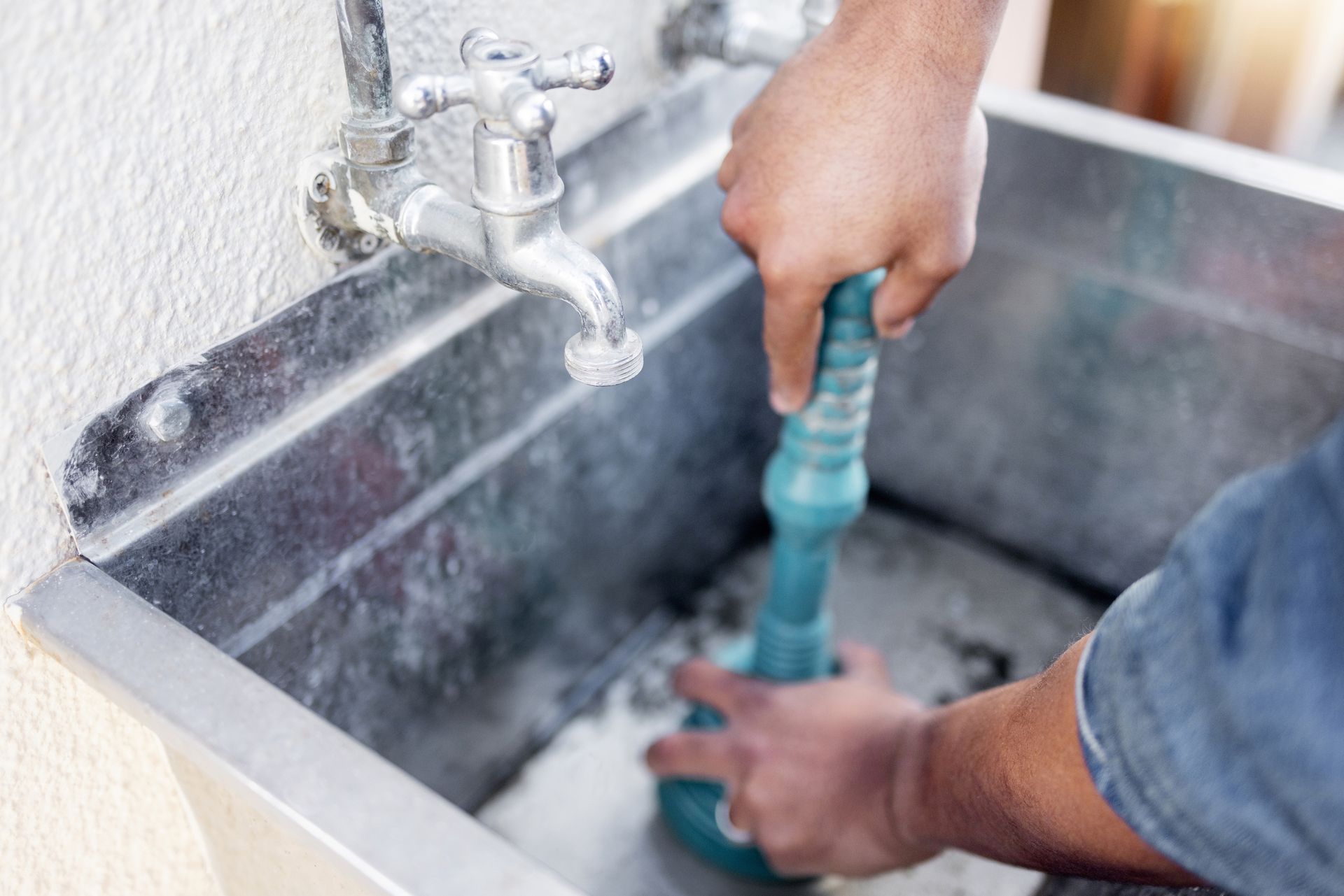 A man is using a plunger to unblock a drain in a sink.