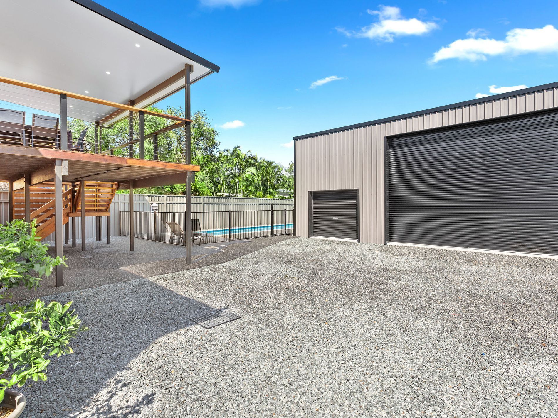 Modern building with covered outdoor deck, gravel courtyard, and large garage-style doors — Wade Adams Constructions in Forster, NSW
