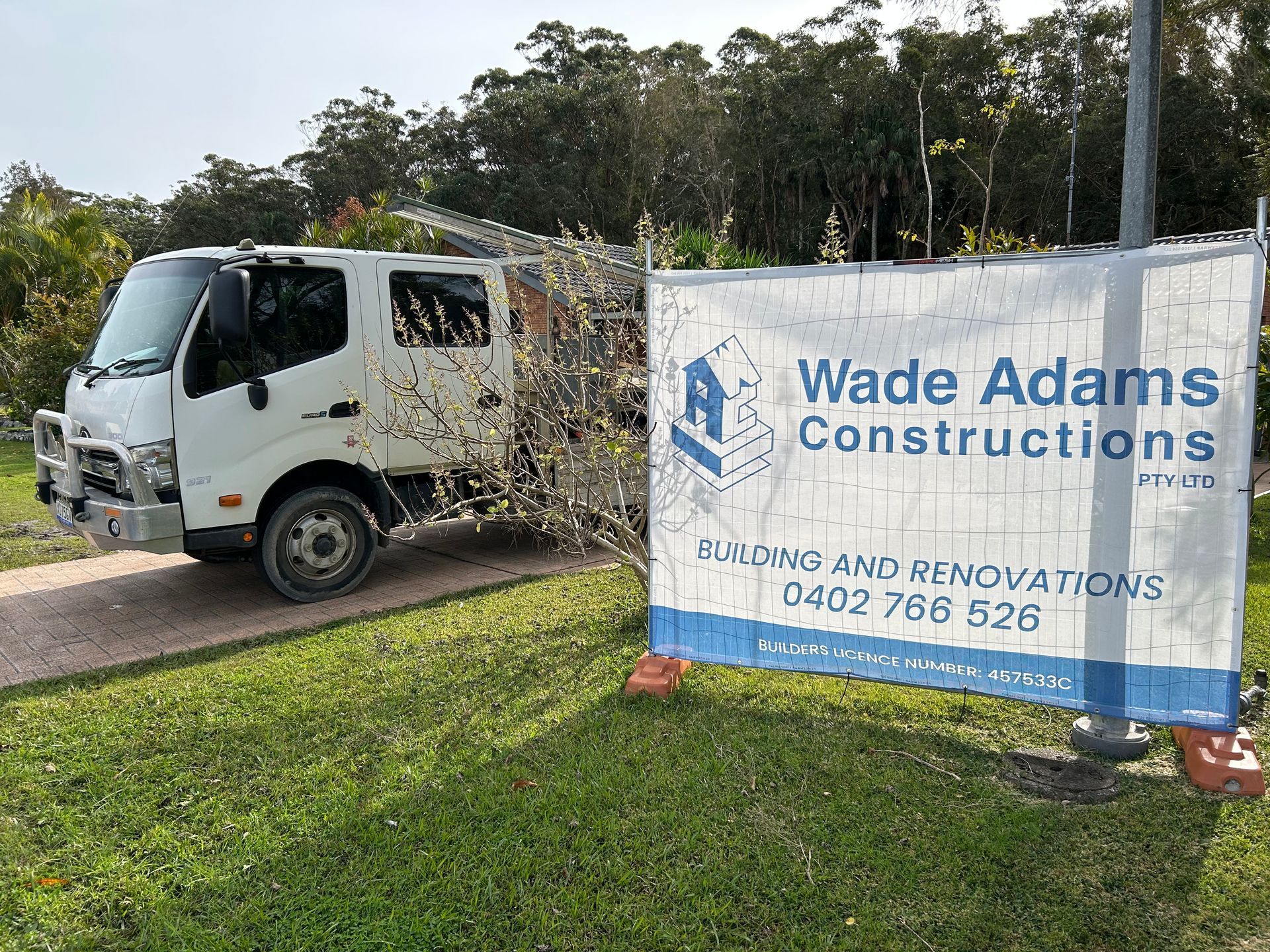 Wade Adams Construction banner beside a white work truck on a grassy roadside — Wade Adams Constructions in Forster, NSW
