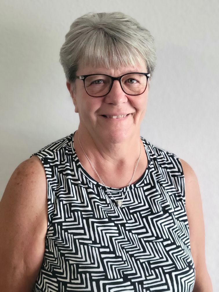 A woman wearing glasses and a black and white shirt is smiling for the camera.