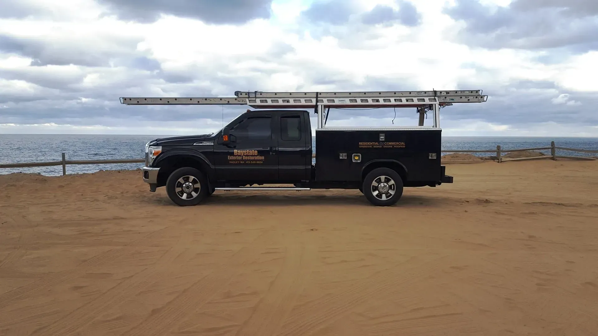 a black truck with a ladder on top of it is parked on the beach