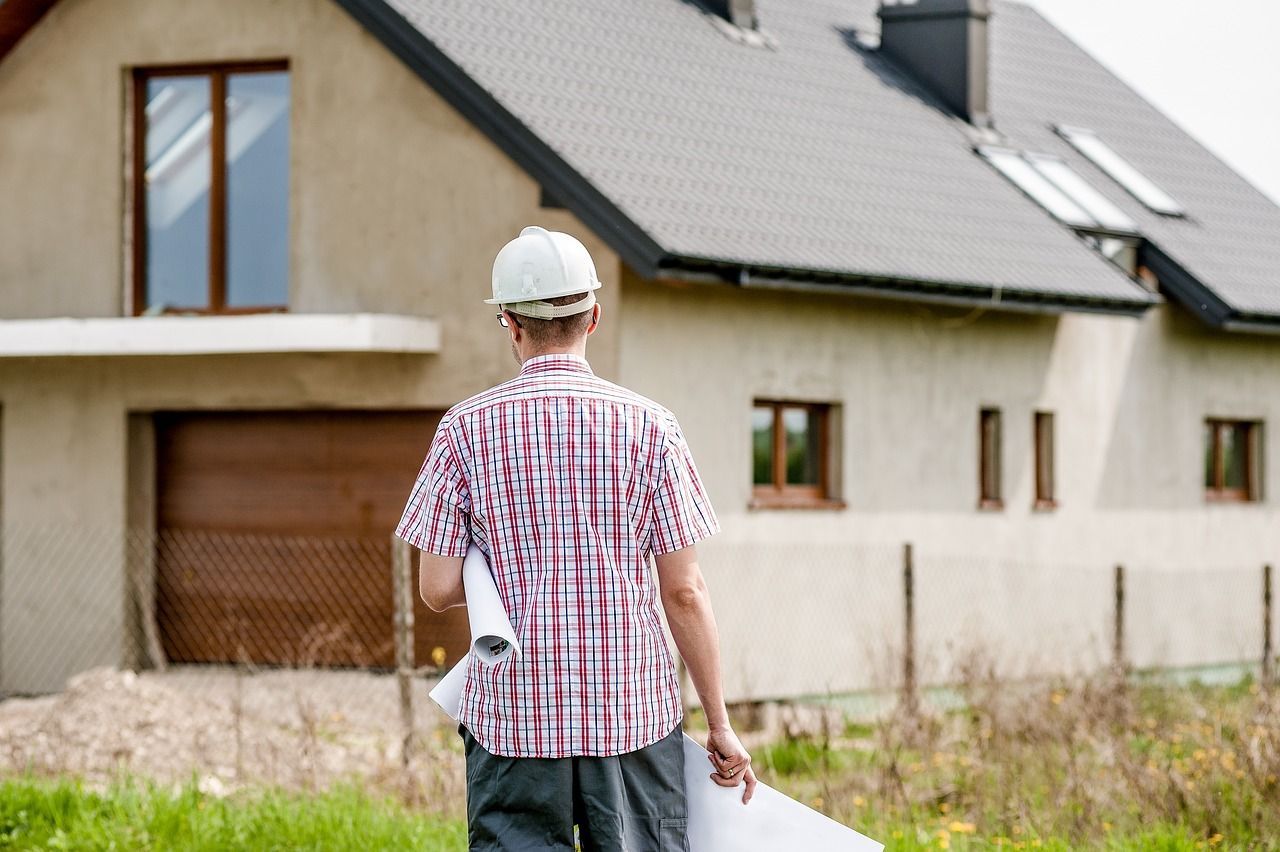 a man wearing a hard hat and holding a blueprint is walking towards a house under construction