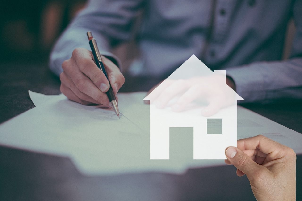 a man is writing on a piece of paper while a woman holds a paper house 