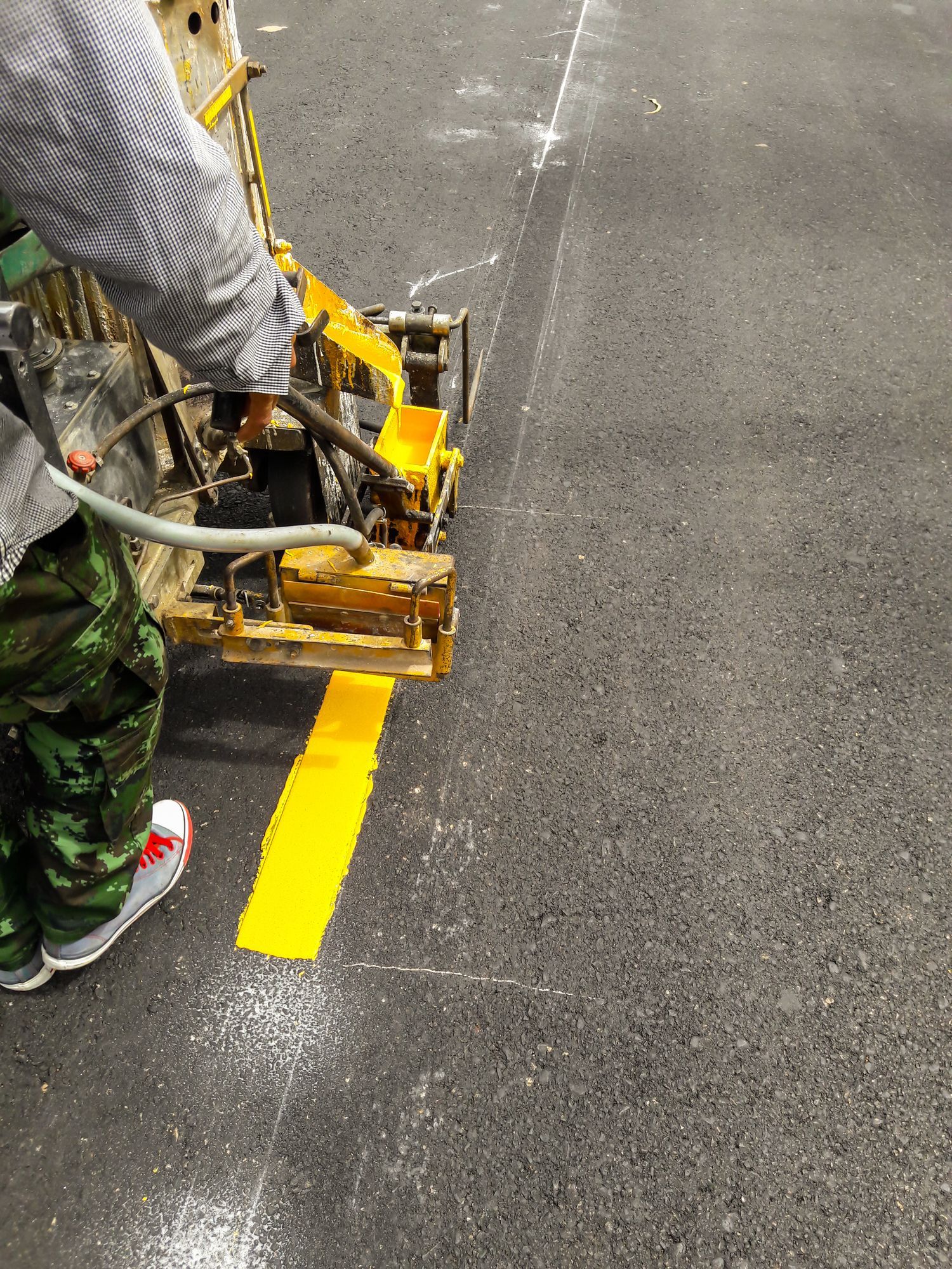 A person is using a machine to paint a yellow line on the ground.