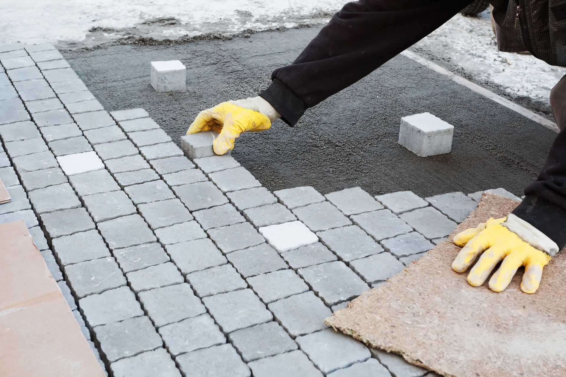 A person wearing yellow gloves is laying bricks on a sidewalk.