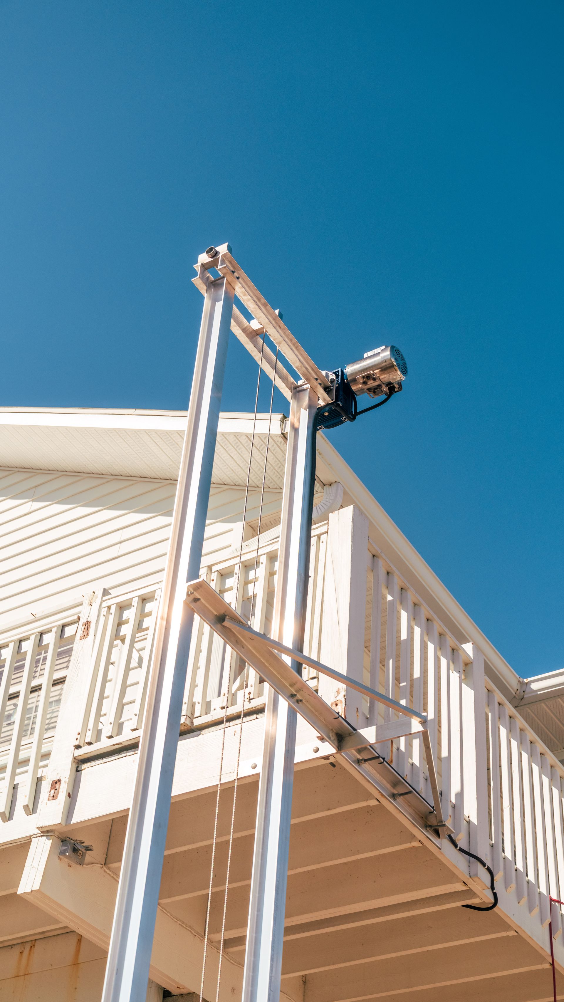Silver boat lift mounted on a white house deck, against a blue sky.