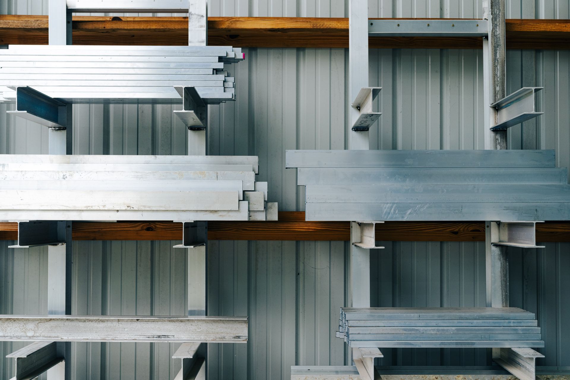 Metal beams stored on shelving against a corrugated metal wall.