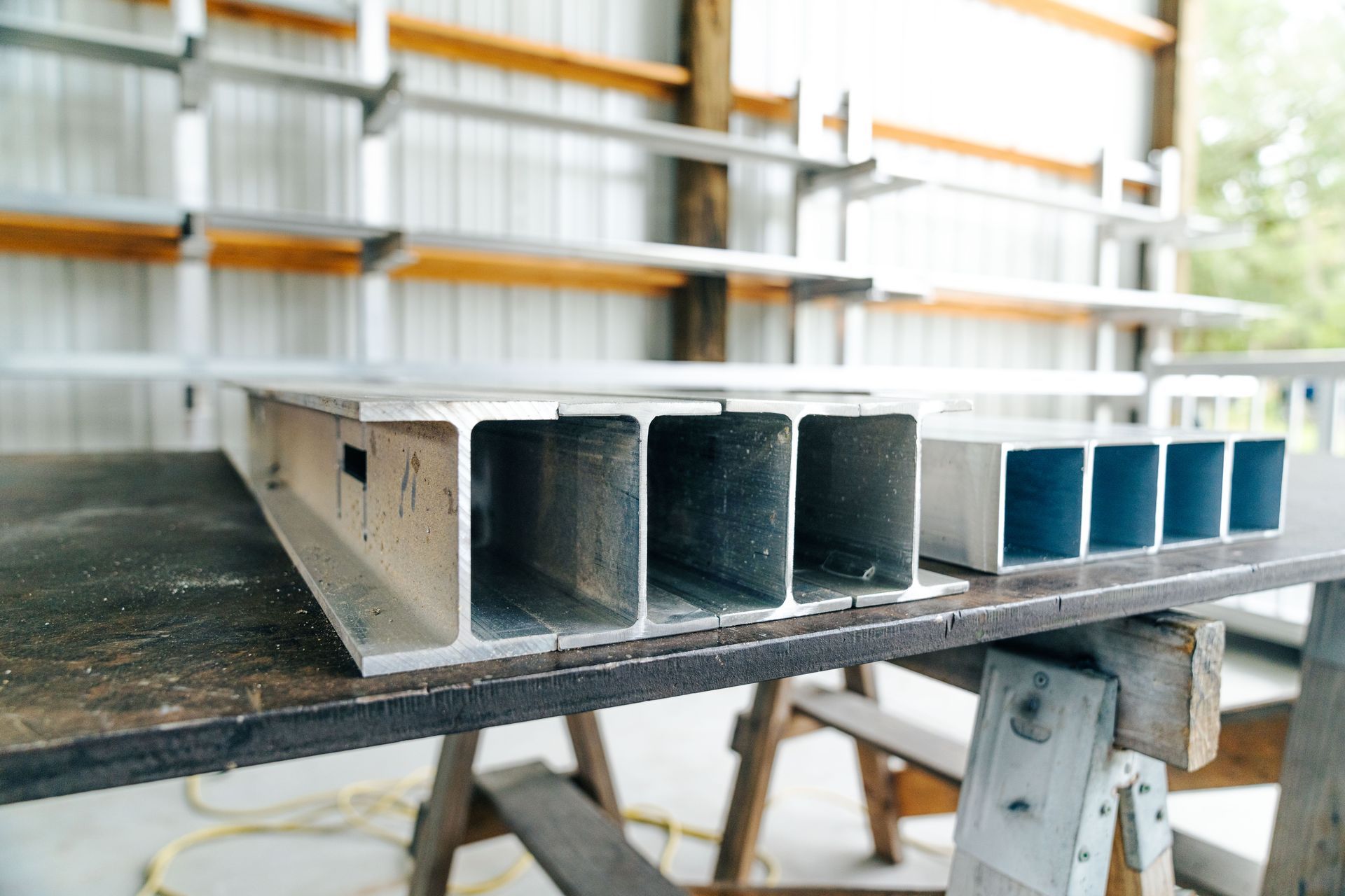 Aluminum beams with multiple channels rest on a workbench in a workshop.