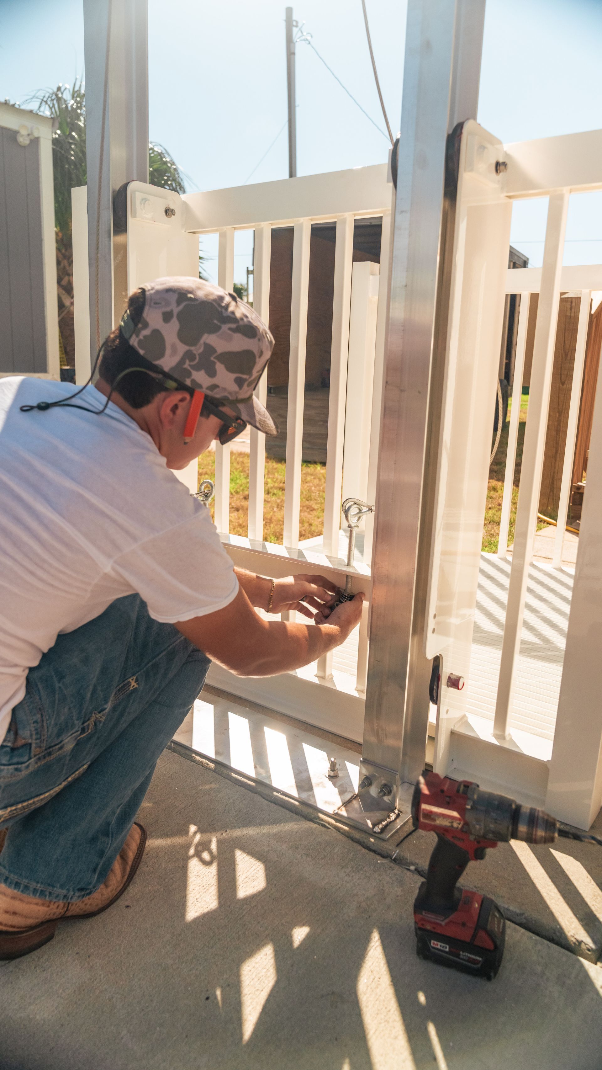 Person in camo hat installing a gate with a power drill outside.