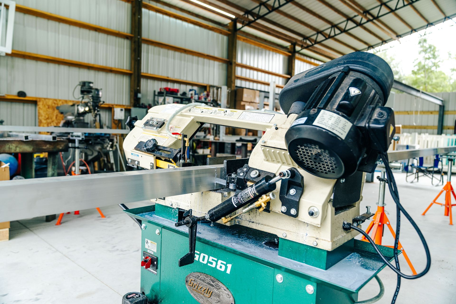 A metal-cutting bandsaw in a workshop, ready to cut a large aluminum beam.