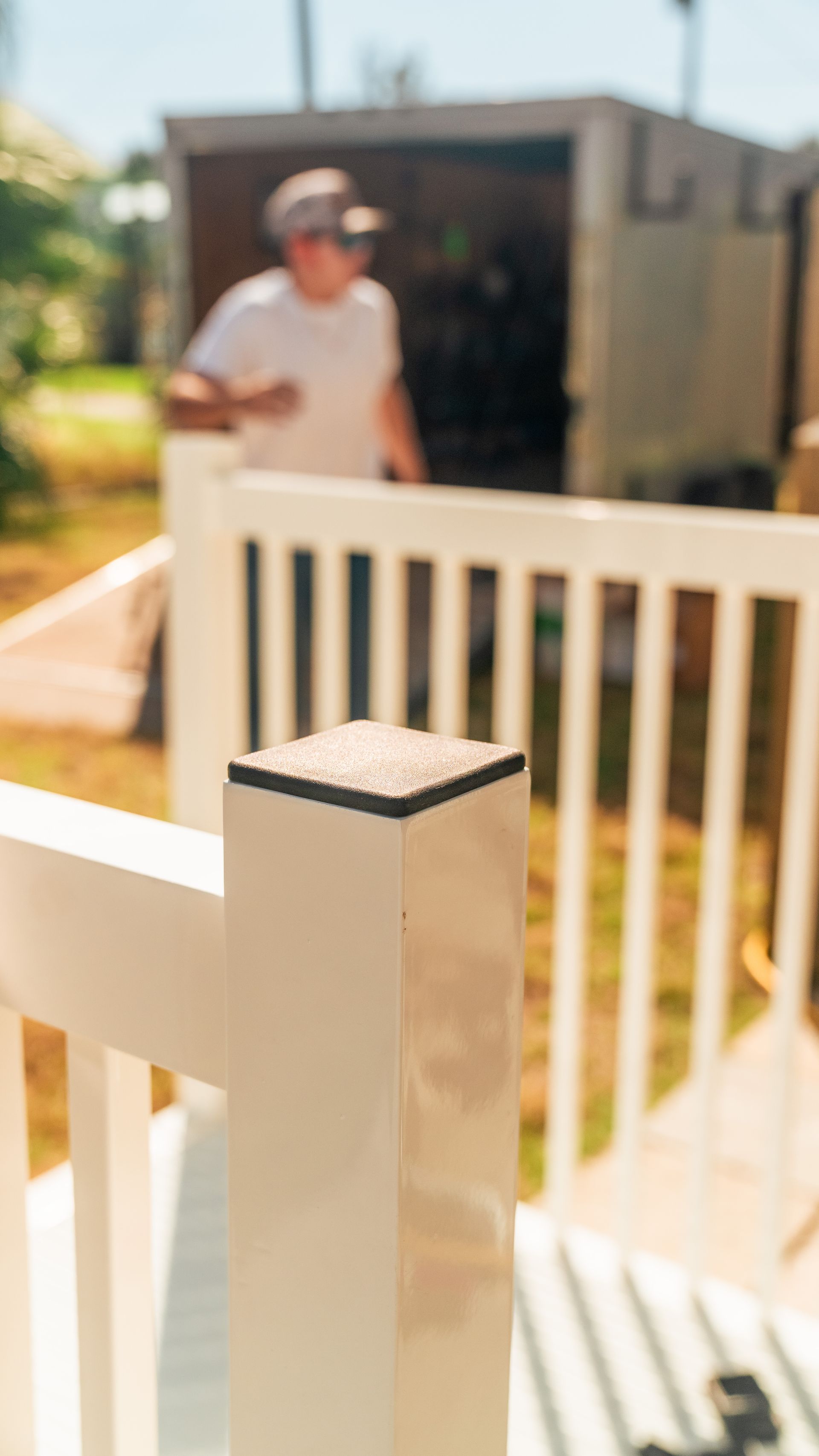 White deck railing post with a person in the background near a shed.