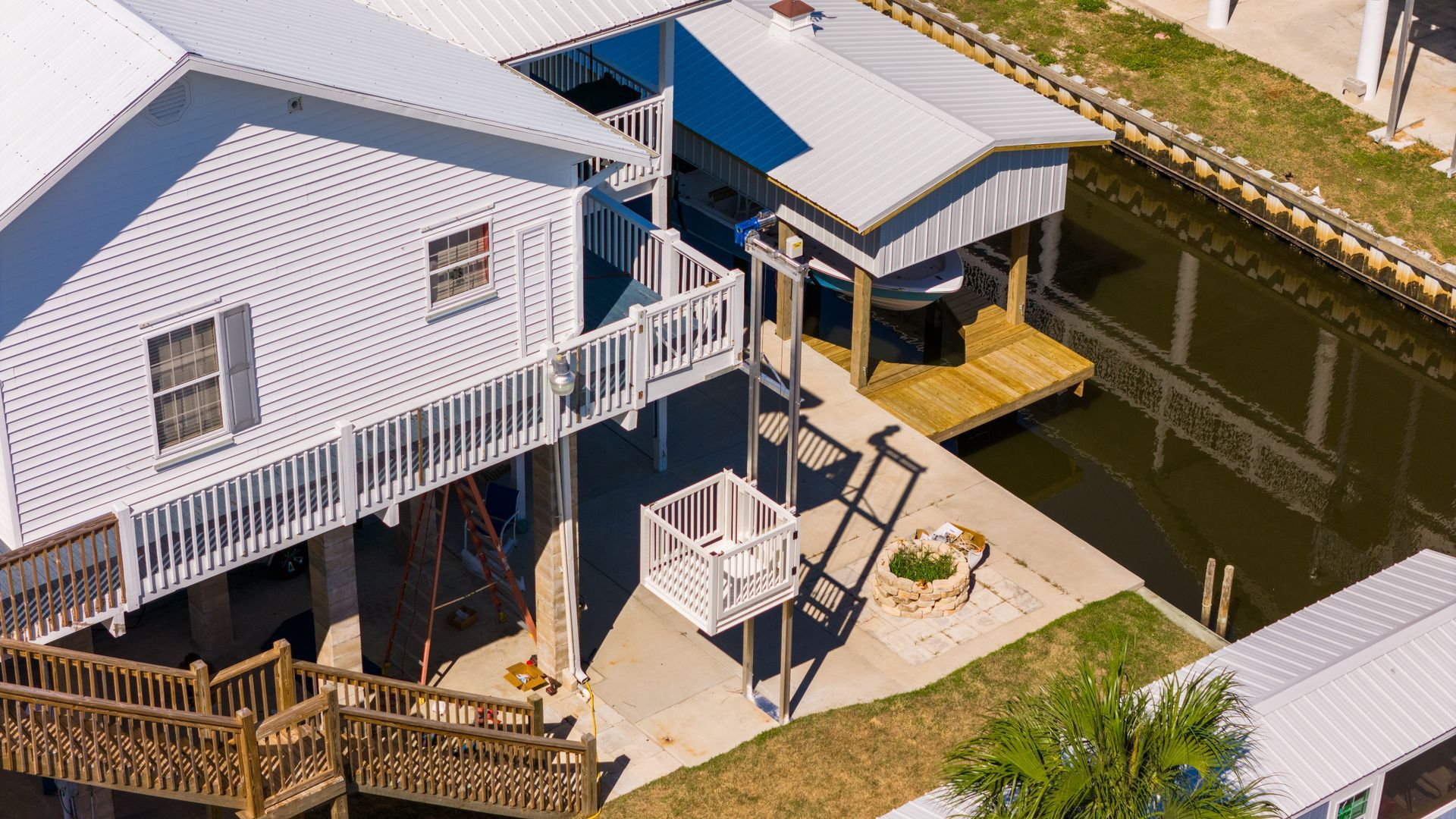 An elevated white house with a boat dock on a canal. Features a lift for accessibility.