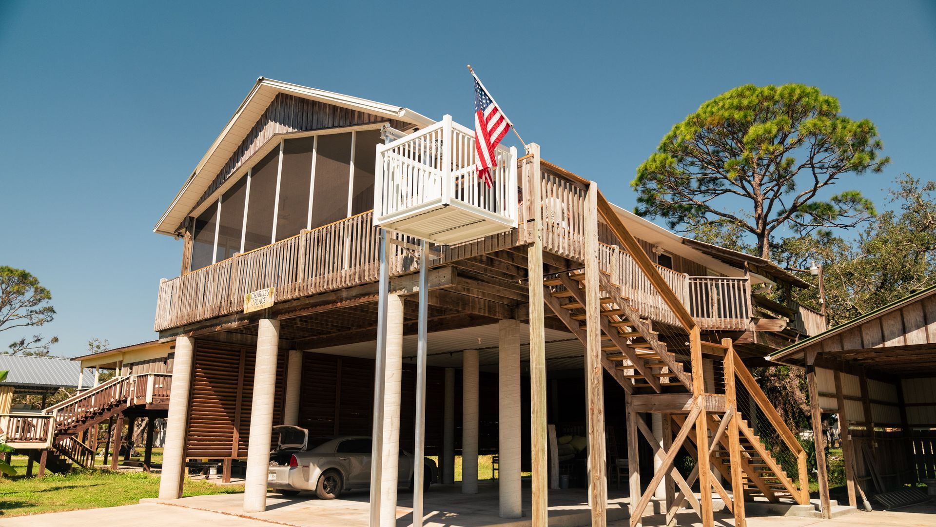 Elevated wooden house with a wheelchair lift and American flag. A car is parked below.