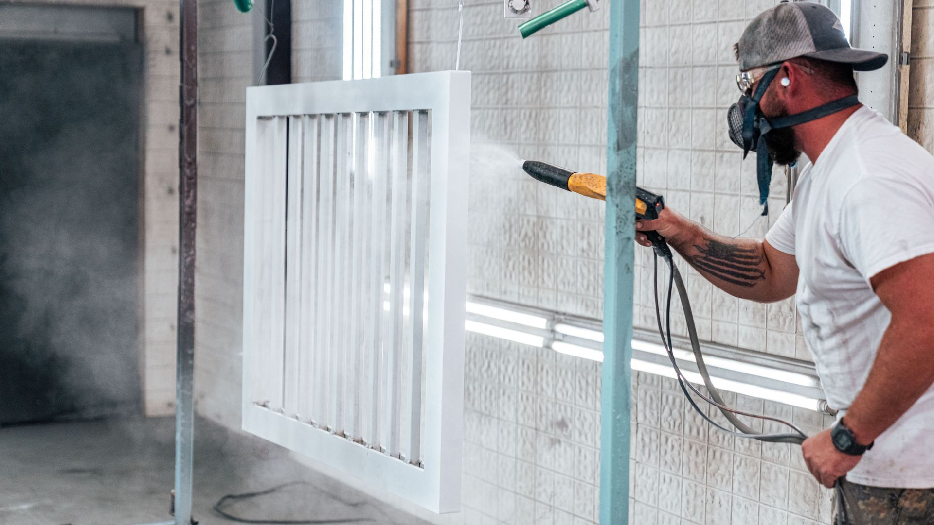 Man in respirator powder coating white metal in a spray booth.