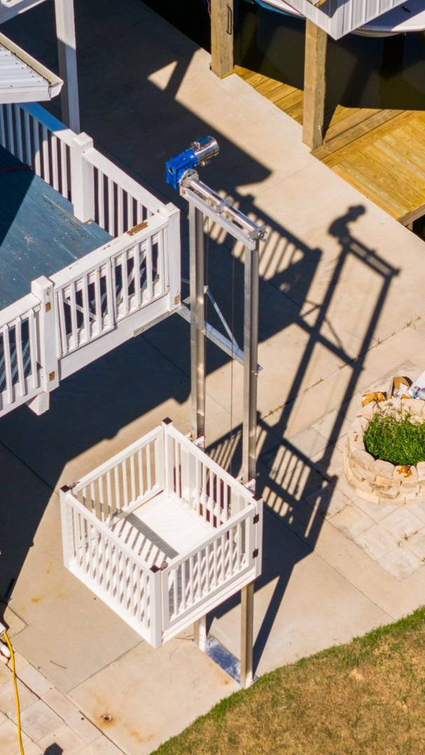 Elevated platform lift next to a deck, for accessibility. White railings, sunny outdoor setting.