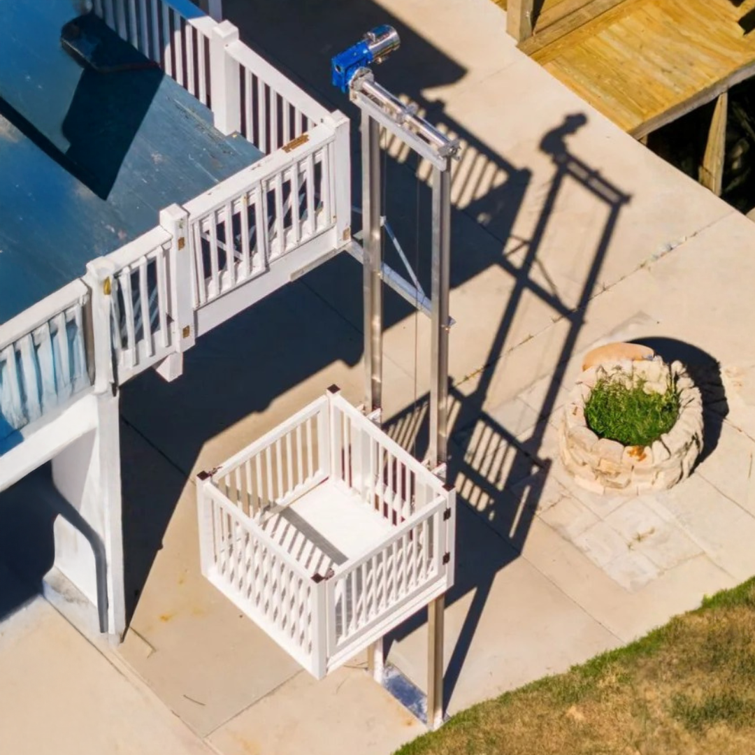 Wheelchair lift installed next to outdoor stairs. Black lift enclosure, beige building, greenery.