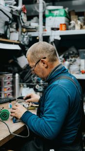 Een persoon in een blauwe jas werkt aan een rommelige werkbank voor 