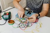 Een persoon die een klein elektronisch projectje met kleurrijke kabels aansluit op een witte tafel.