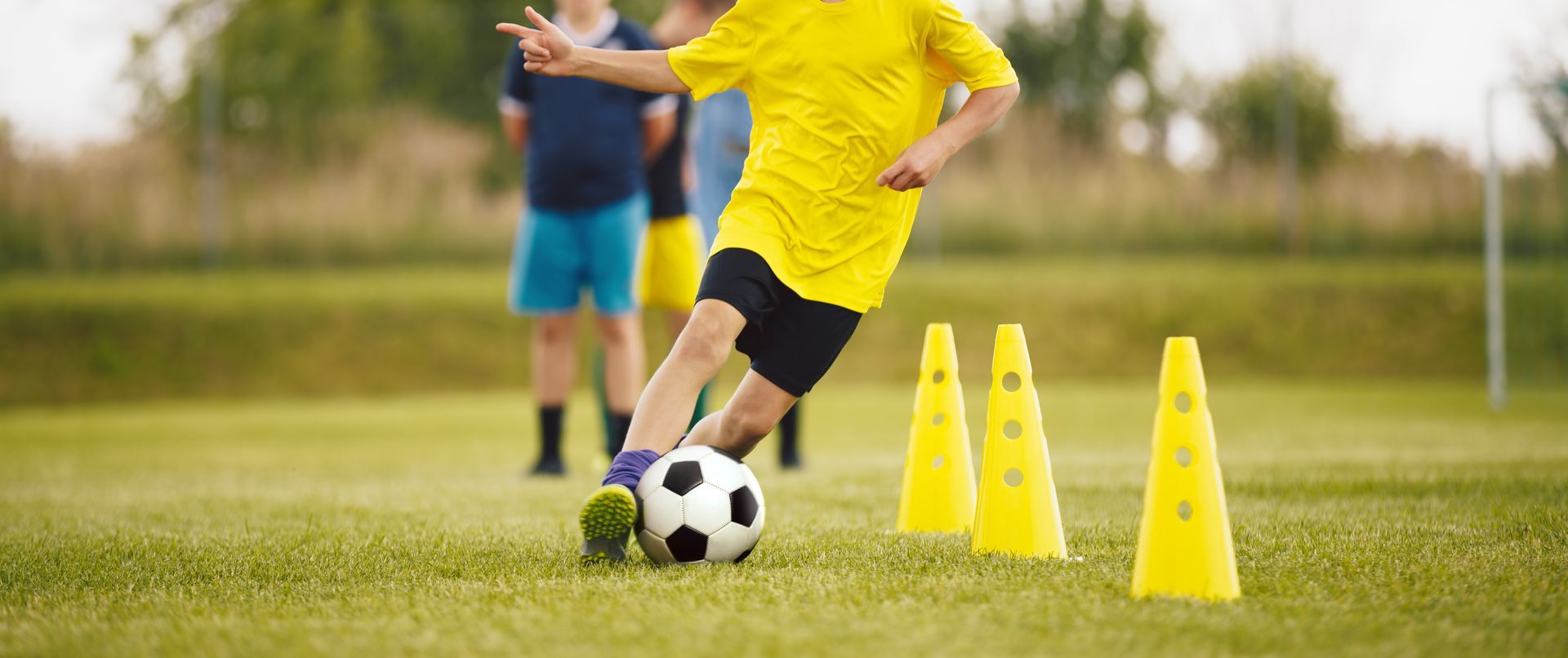 young soccer player dribbling a soccer ball around yellow cones