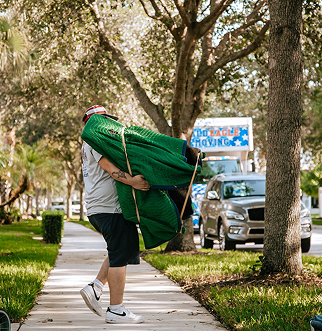 A man is carrying a green couch down a sidewalk.