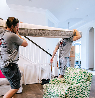 Two men are carrying a large rug over their heads in a living room.