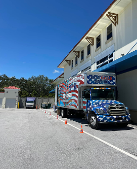 A red white and blue truck is parked in front of a building.