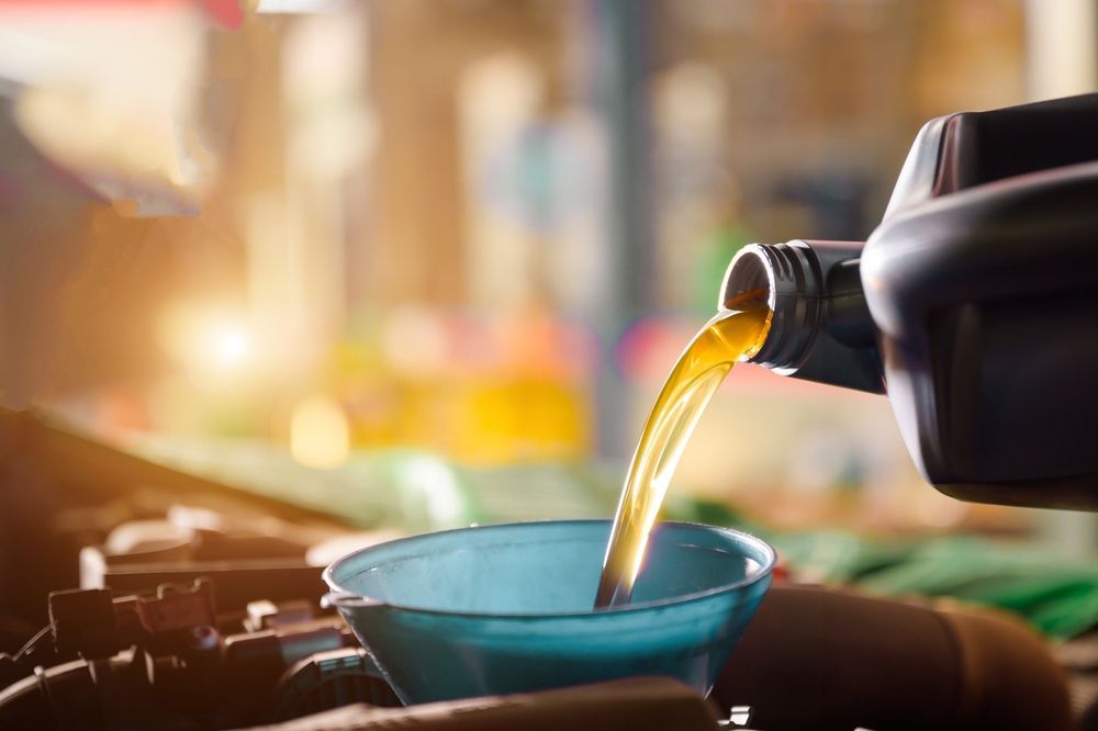 Oil being poured from a black container into a blue funnel in a car engine bay.