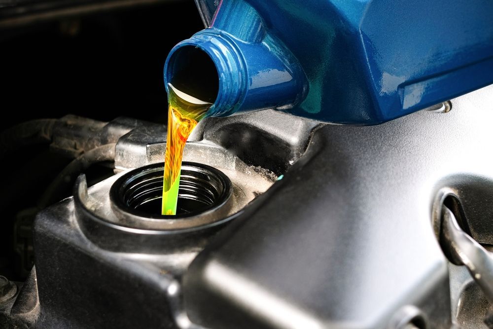 Pouring motor oil into a car engine; blue oil container, silver engine components, black fill hole.