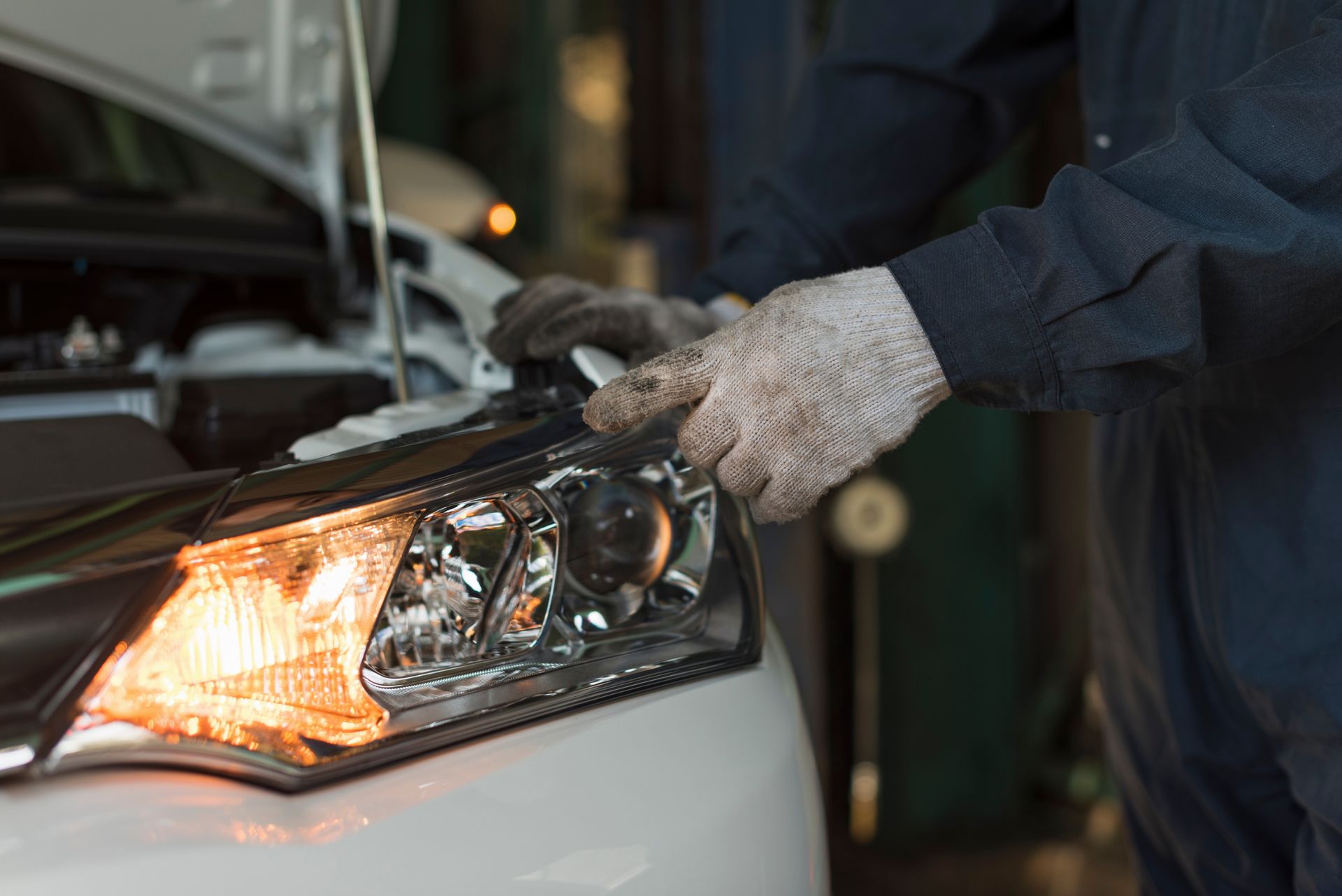 Mechanic replacing a car headlight. The car is white, and the light is orange.