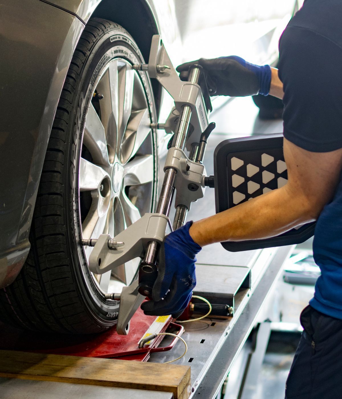 A mechanic in gloves attaches a wheel alignment sensor to a car tire in an auto repair shop.