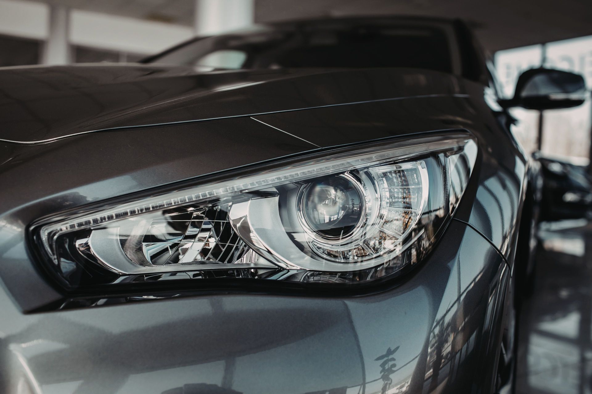 Close-up view of the front headlight and hood of a dark grey sedan in a dealership showroom.