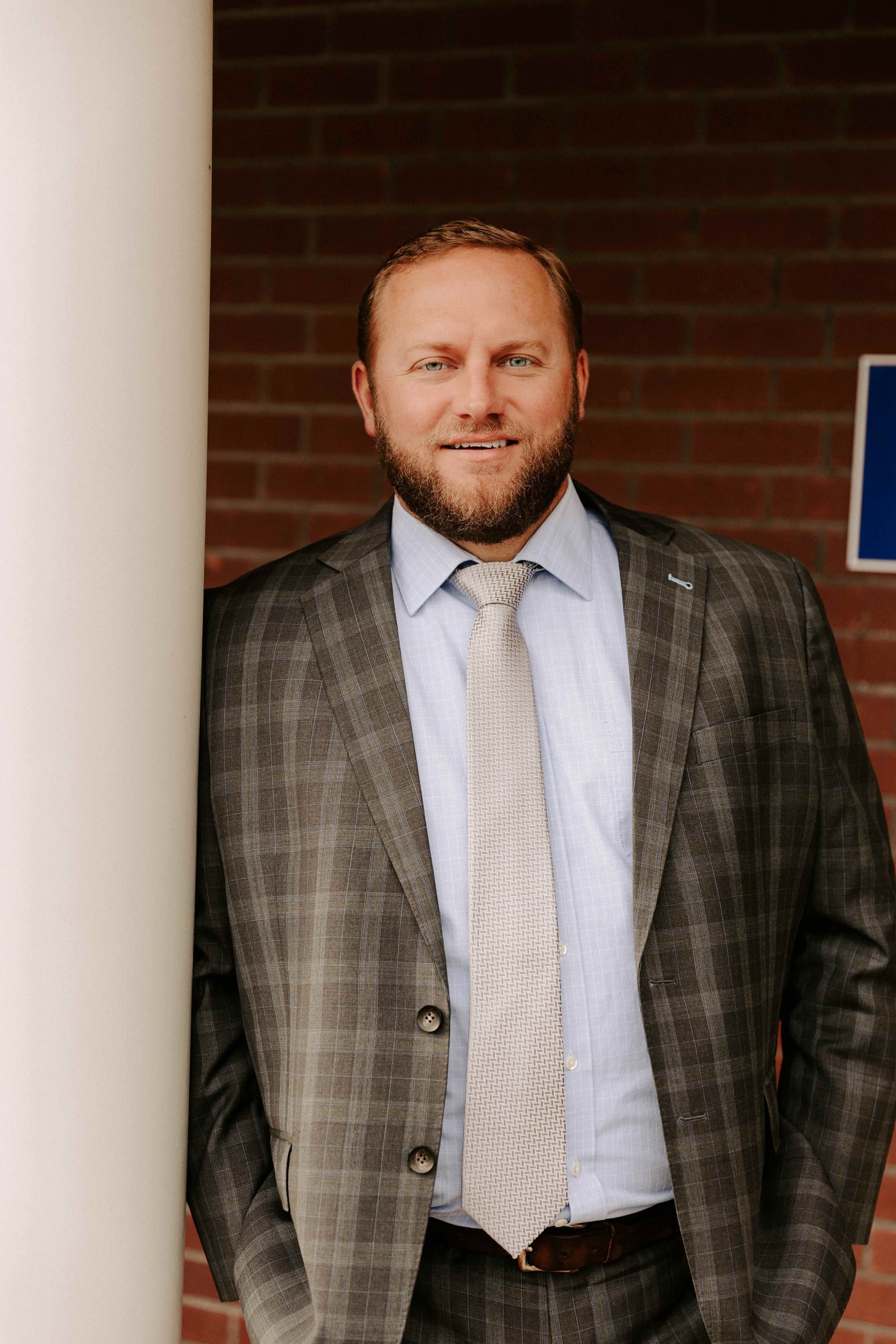 A criminal defense attorney in a suit and tie is standing next to a pillar.
