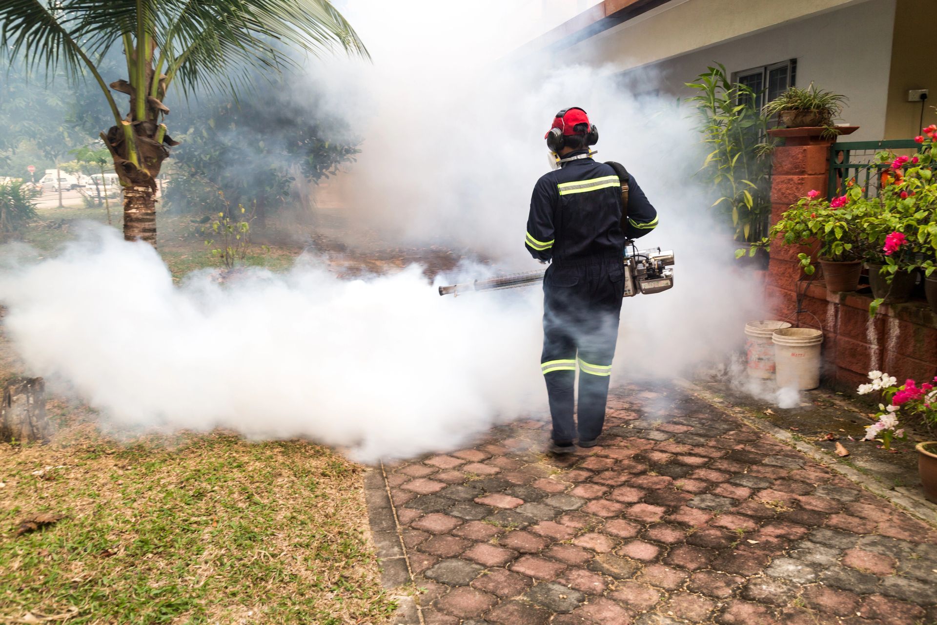 Firefighter in black gear sprays extinguisher foam outside a house, filling the yard with white smoke.