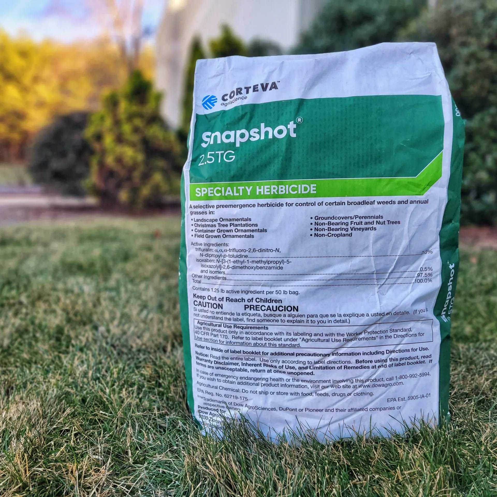 A green and white bag of Snapshot 2.5TG specialty herbicide stands on grass.