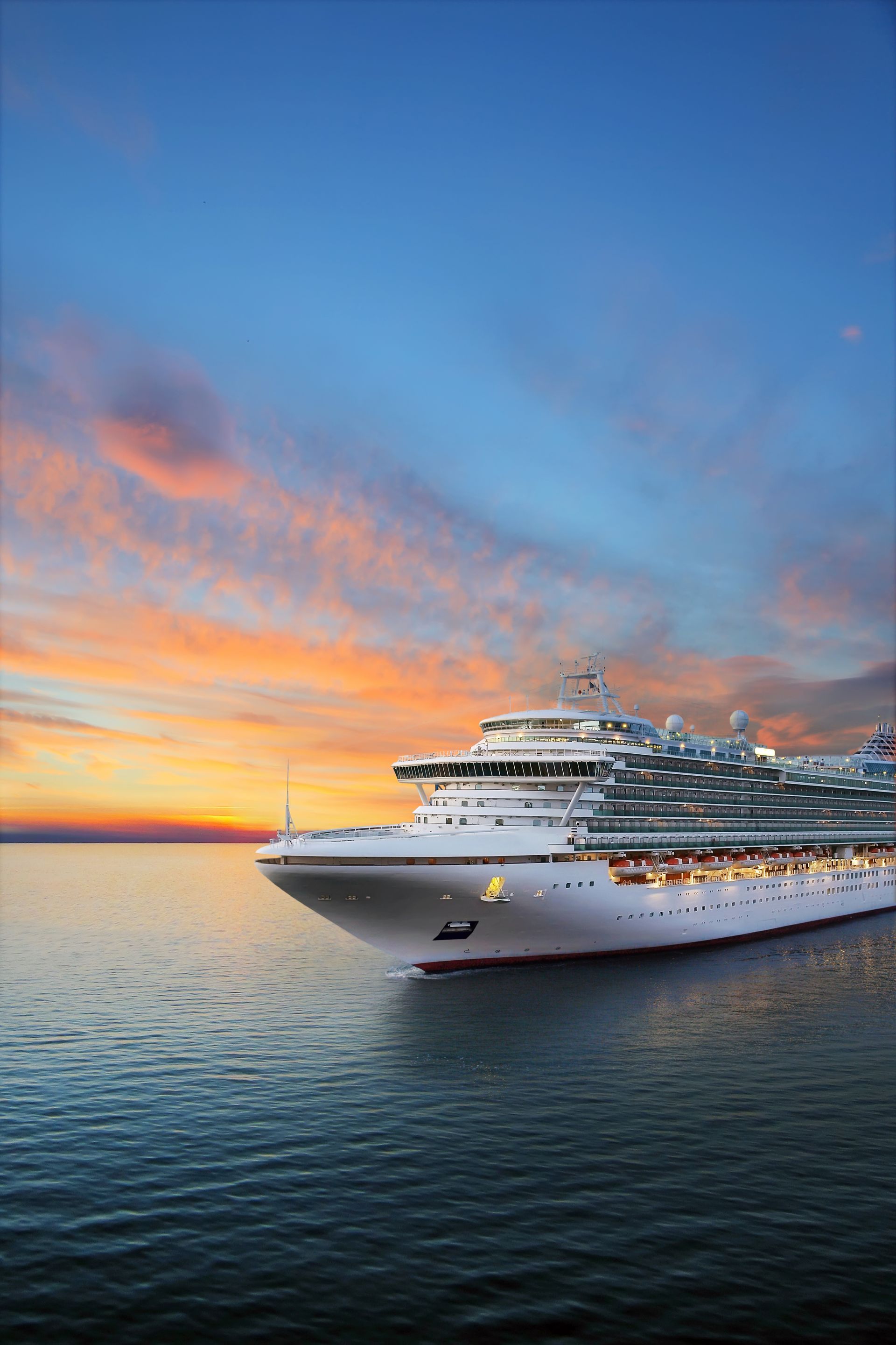Cruise ship sails on calm ocean at sunset, orange and blue sky.