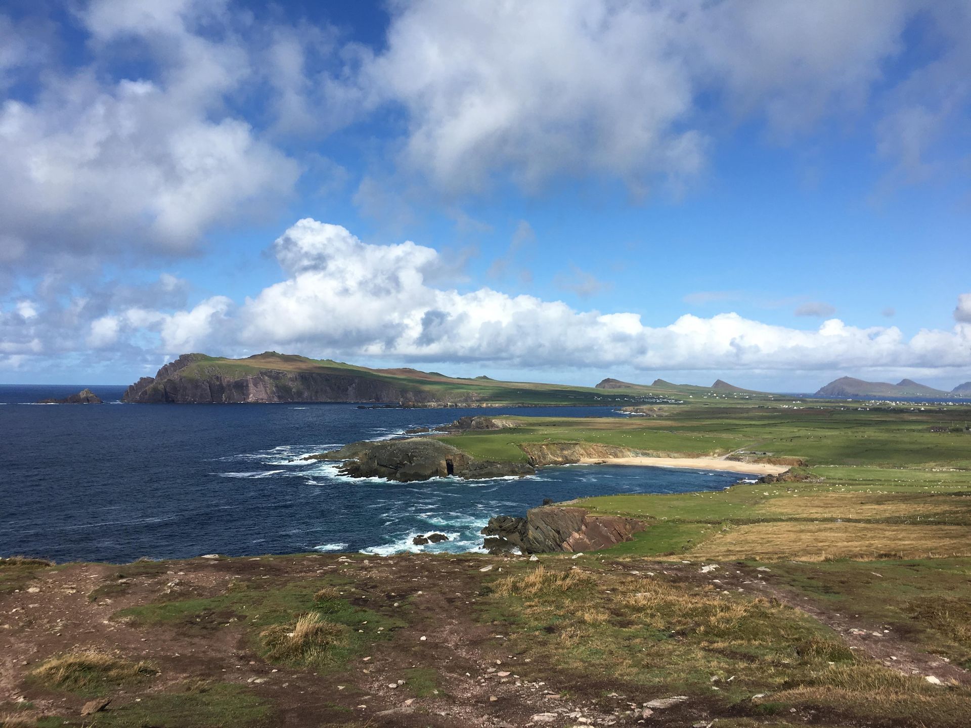 Coastal landscape with blue water, green land, and a partly cloudy sky.