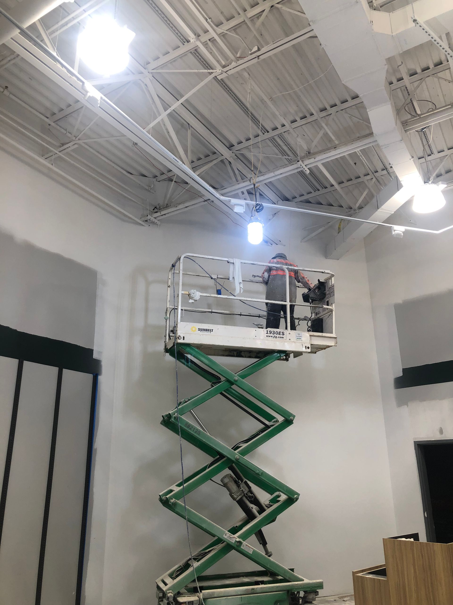 A man is standing on a green scissor lift in a room.