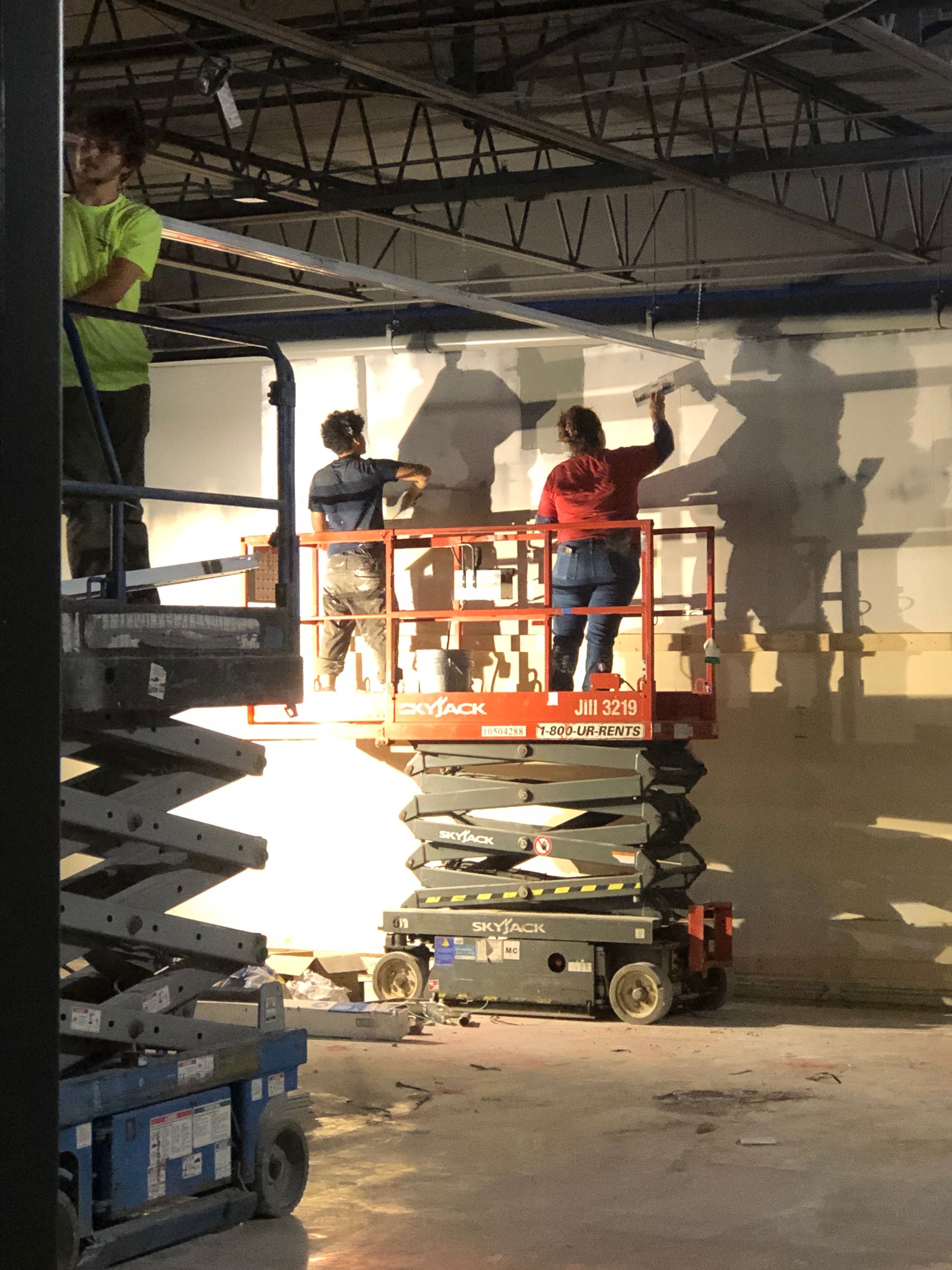 A man and a woman are painting a wall on a scissor lift