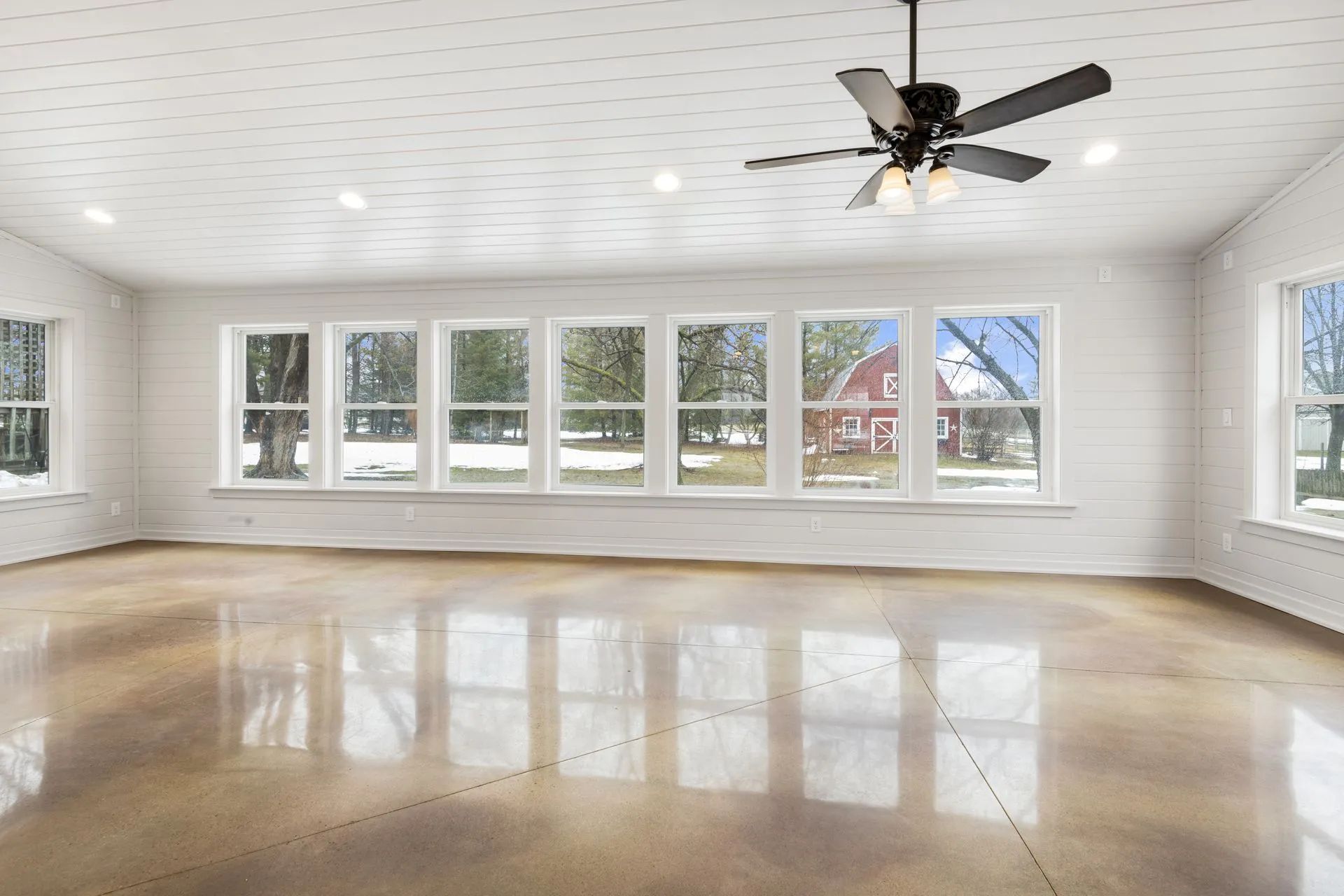 A large empty room with a ceiling fan and lots of windows.