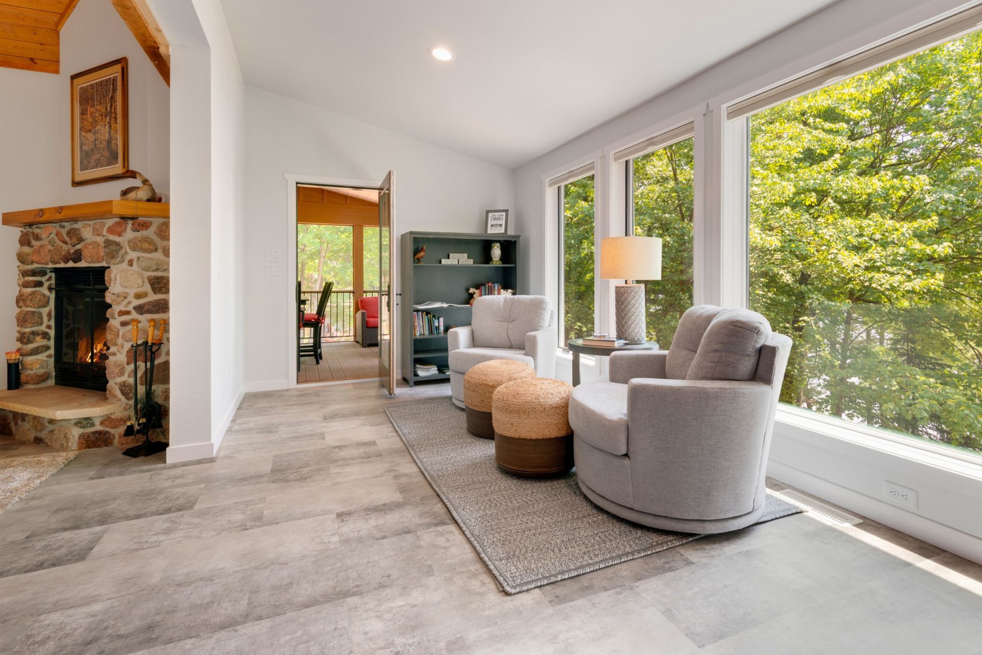 A living room with a fireplace , chairs , ottomans and a large window.