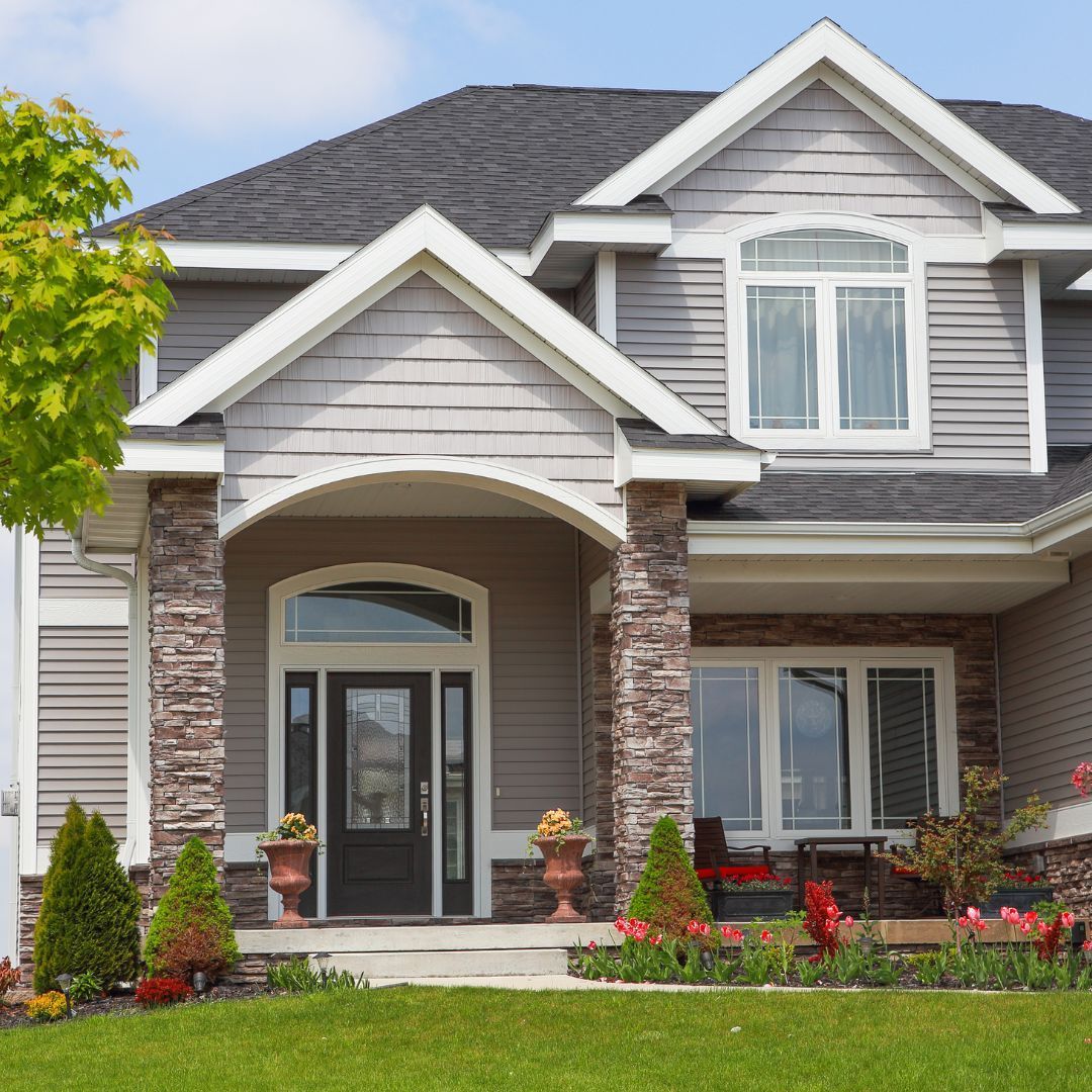 A large gray and white house with a lush green lawn in front of it.