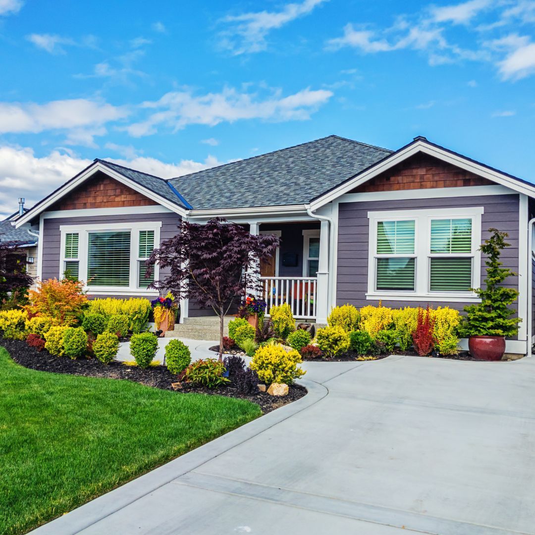 A gray house with a concrete driveway and a lush green yard.
