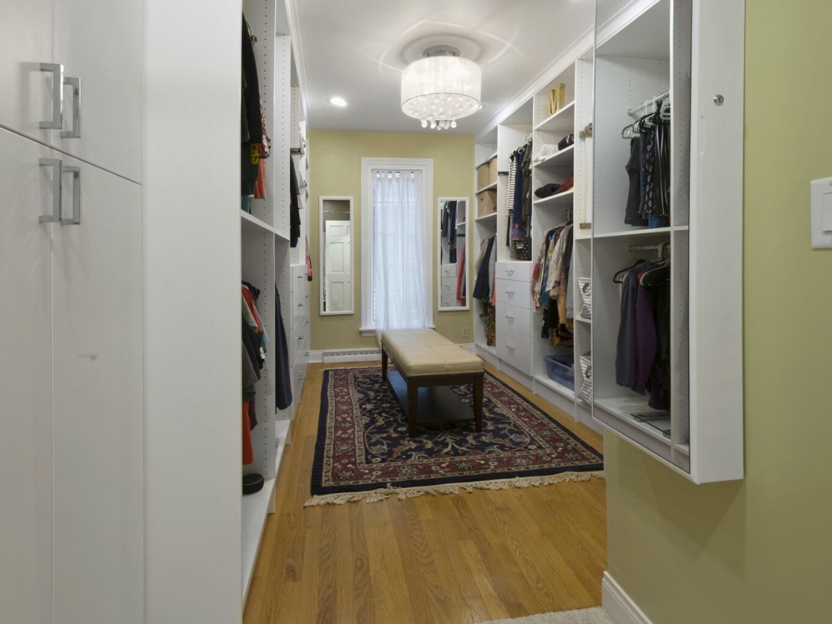 A walk in closet with lots of clothes and a bench.