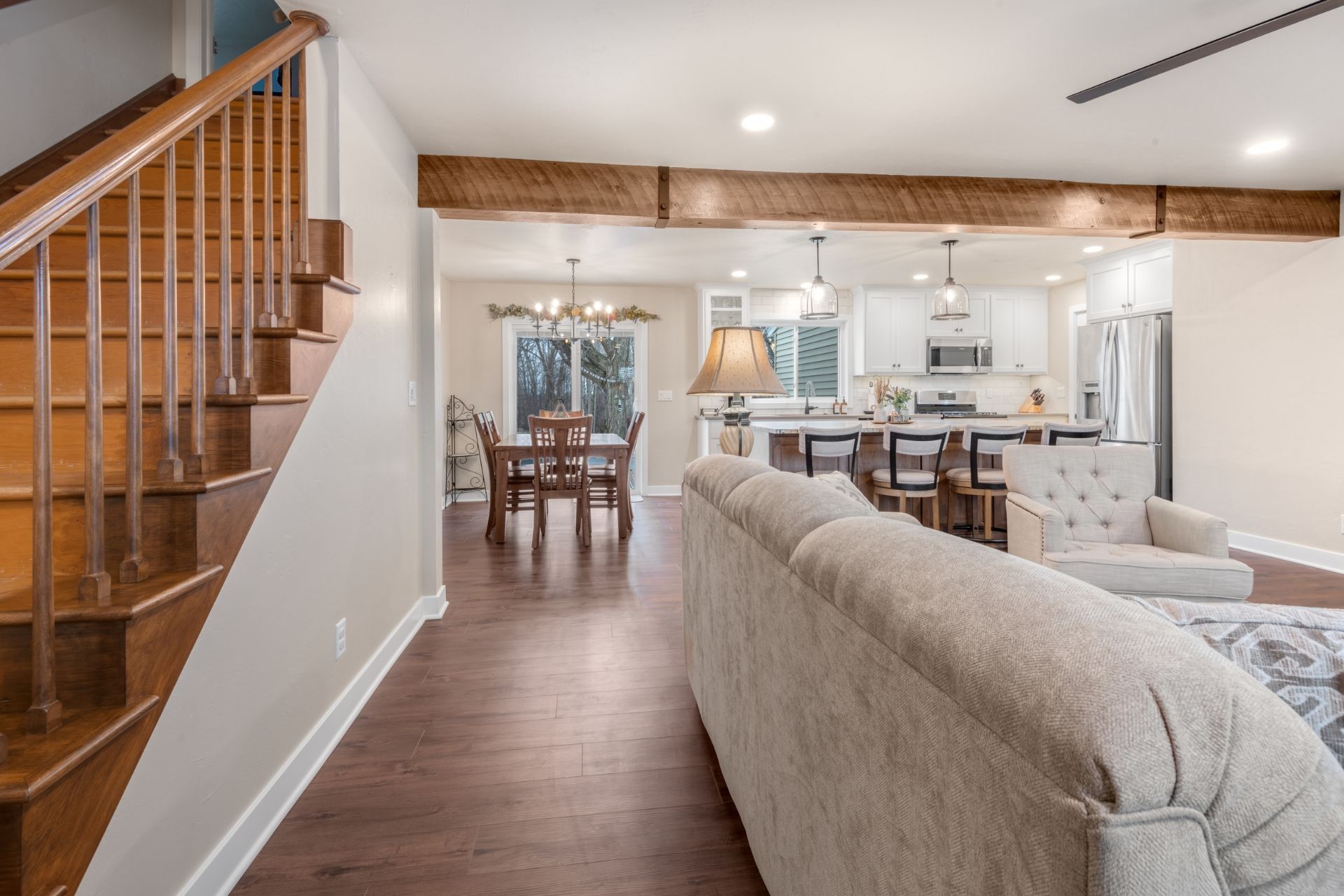A living room with a couch , chairs , stairs and a kitchen.