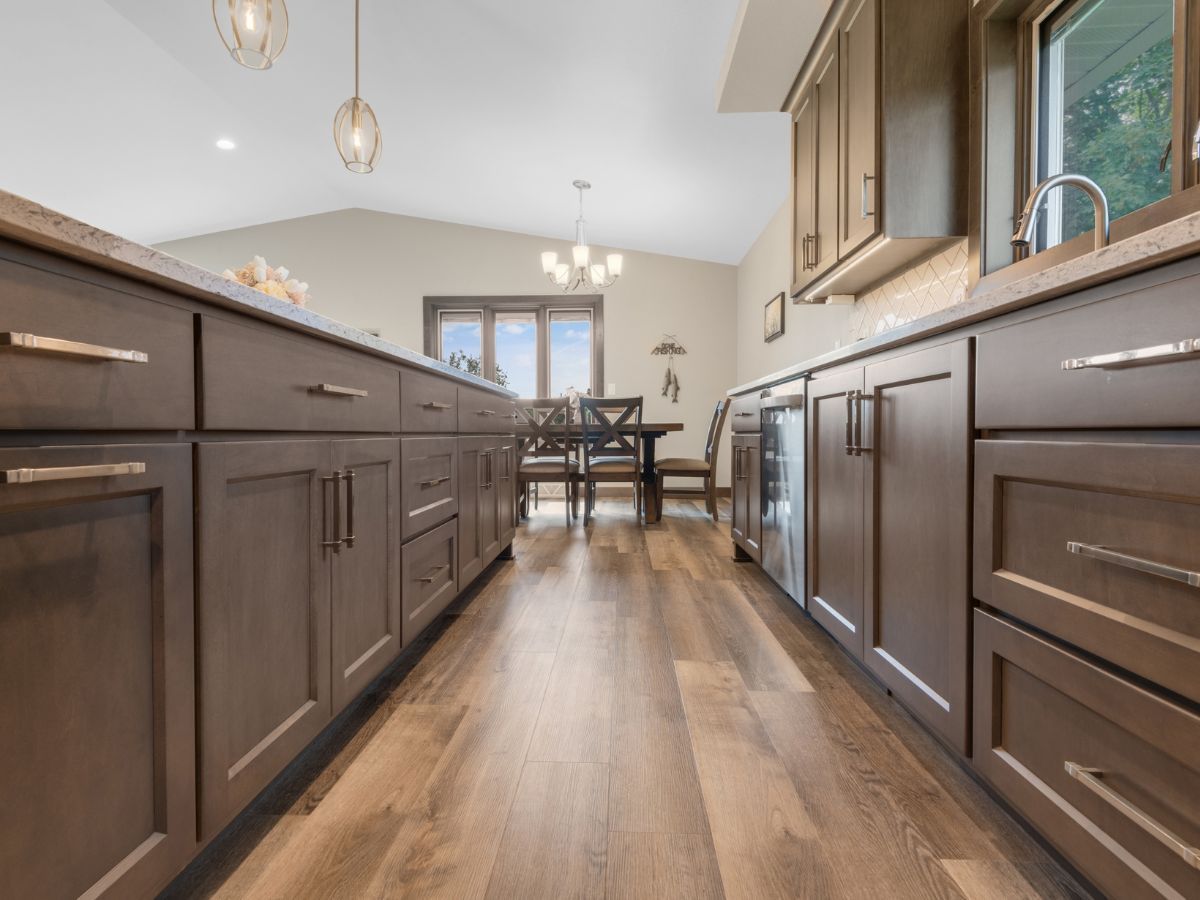 A kitchen with brown cabinets and hardwood floors leading to a dining room.