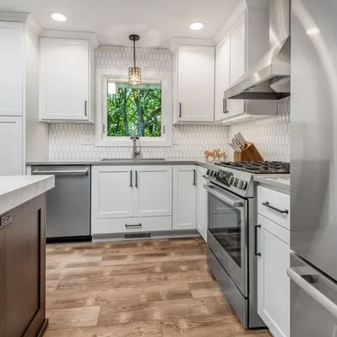 A kitchen with white cabinets , a stove , a refrigerator , and a window.