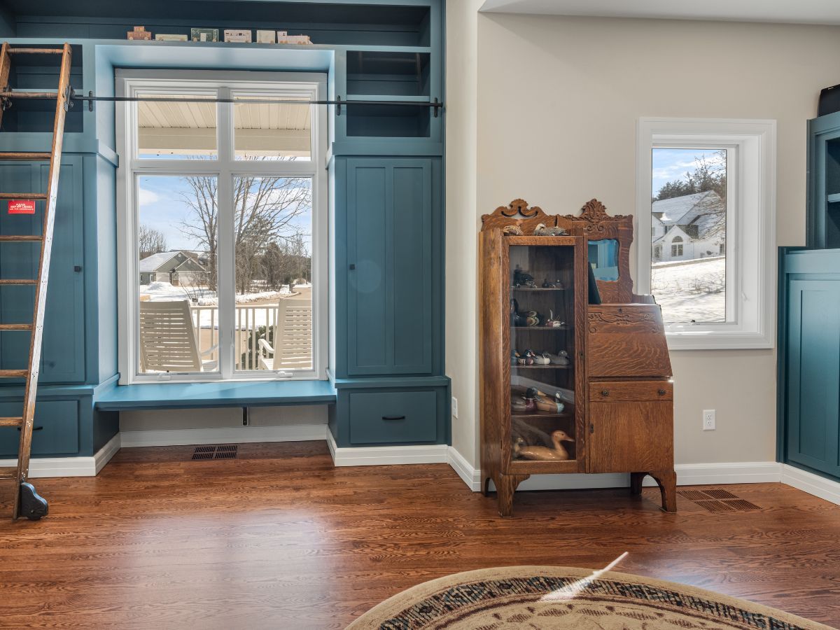 A living room with hardwood floors , blue cabinets , a ladder , and a window.