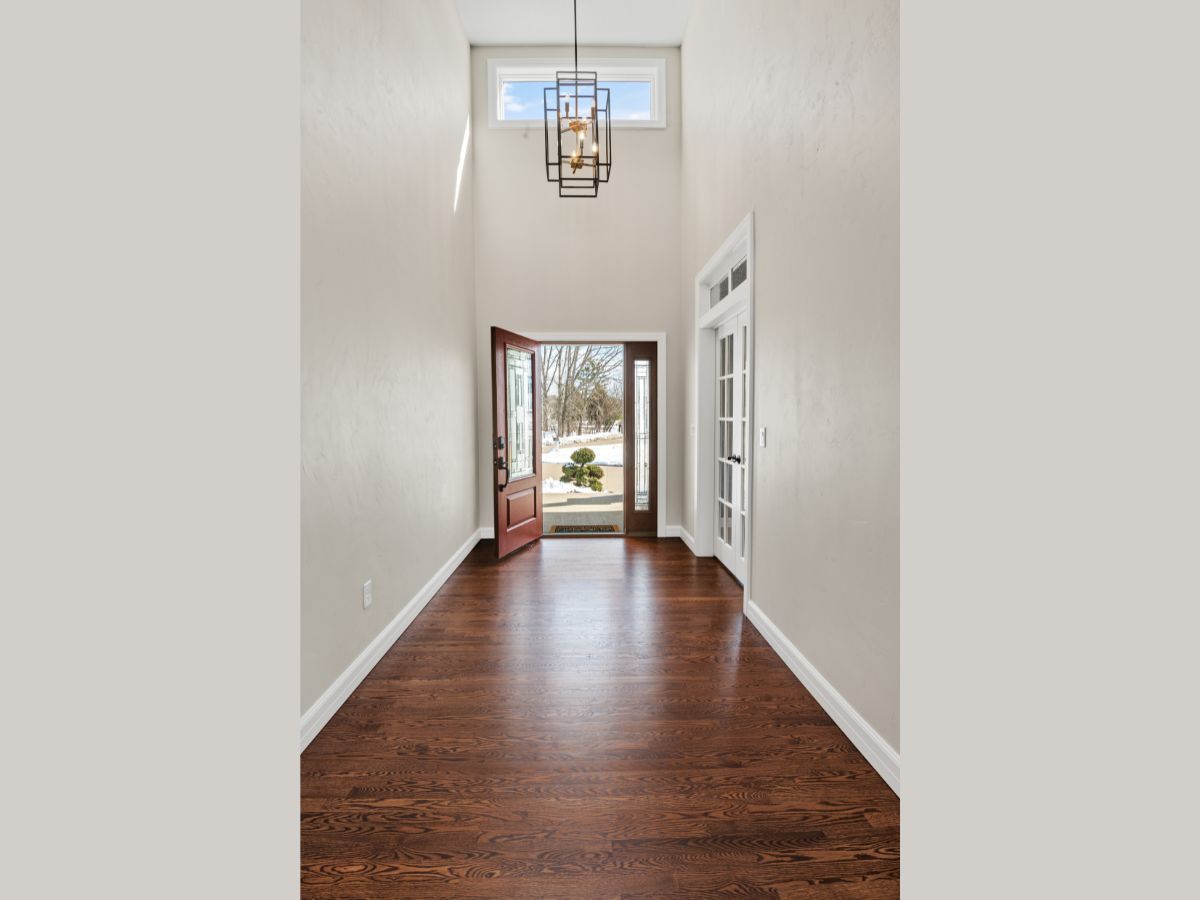 A long hallway with hardwood floors and a chandelier hanging from the ceiling.