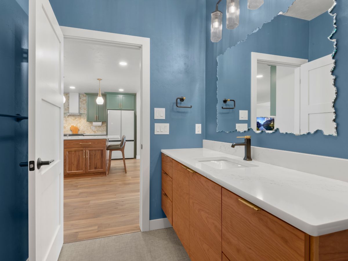 A bathroom with blue walls , wooden cabinets , a sink and a mirror.