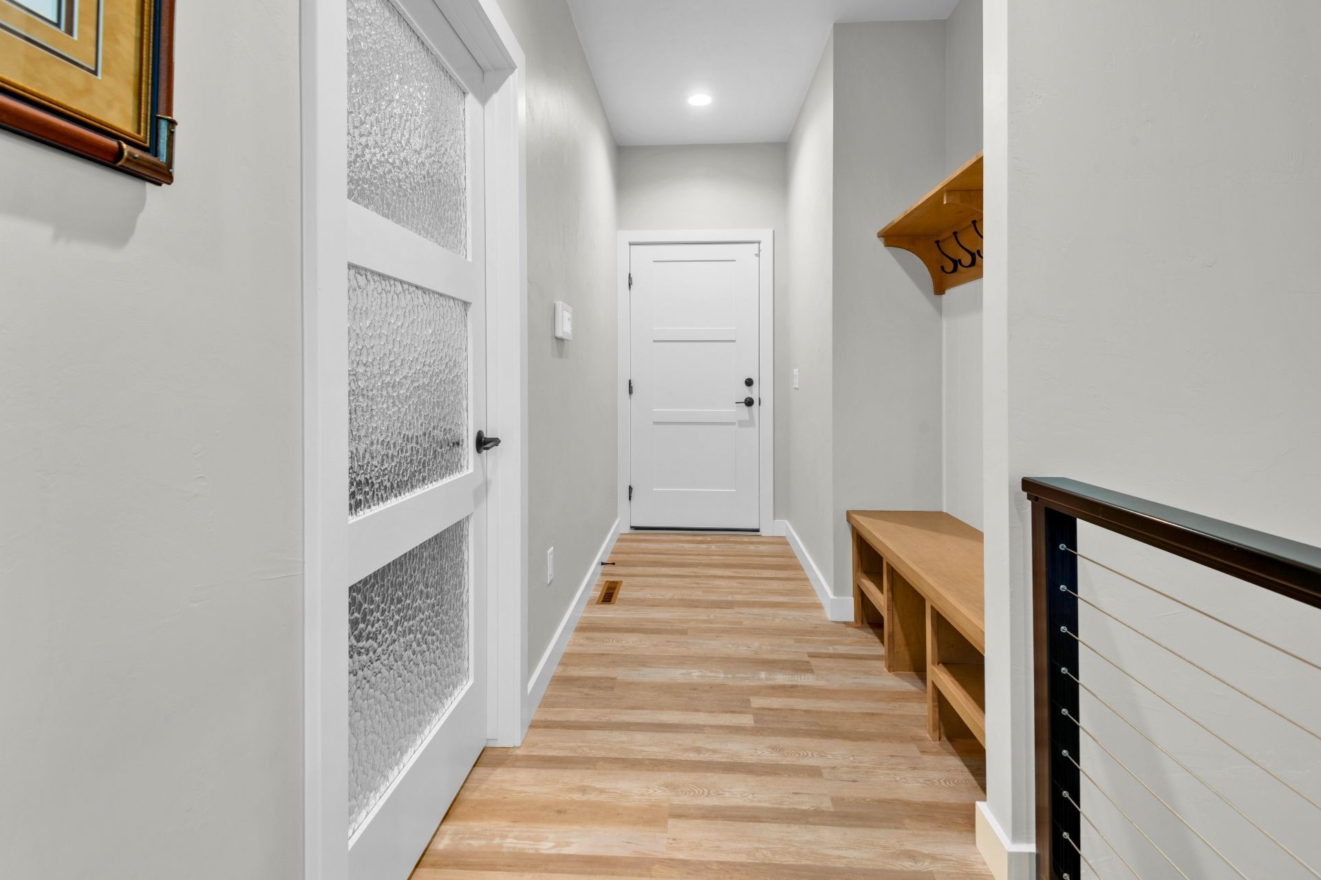 A hallway with hardwood floors , a white door , and a bench.
